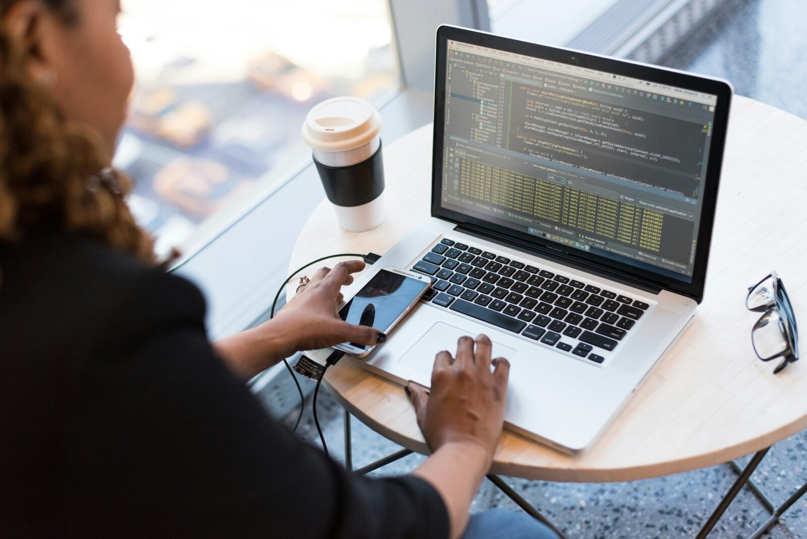 A Hewani team member working at a laptop by a window, coffee in hand